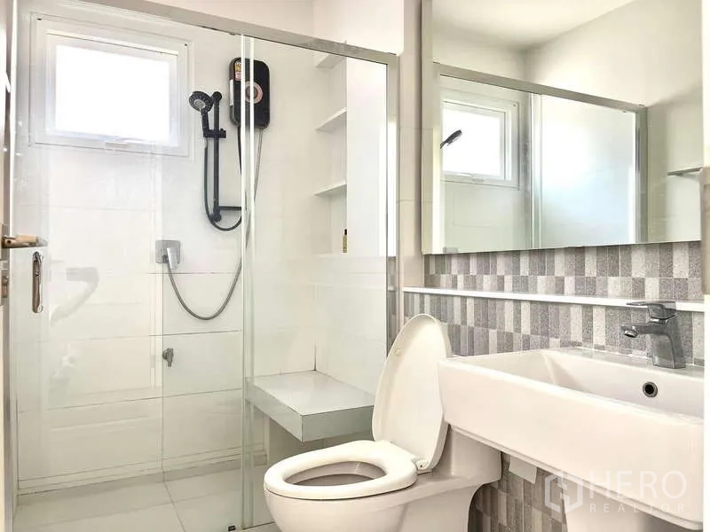Detached House for rent in Prawet, Bangkok - Clean bathroom with glass-enclosed shower, handheld shower, bench seat and wide mirror.