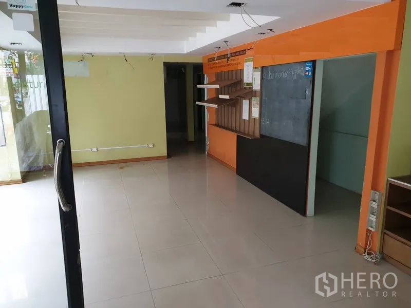Retail Space for rent in Watthana, Bangkok - Open-plan ground floor retail interior with tiled flooring, glass entry door, shelving and an orange feature wall.