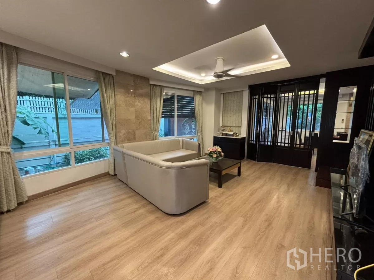 独立式住宅 出租在Bang Kapi, Bangkok - 开阔客厅，L 型沙发、大窗与层叠吊顶。