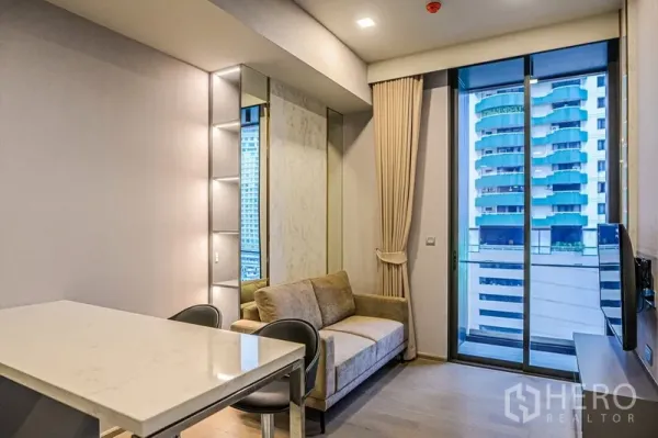 Condominium for rent in Watthana, Bangkok - Living room with beige sofa, floor-to-ceiling windows and a balcony overlooking the city skyline.