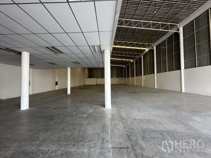 Factory for rent in Khlong Luang, Pathum Thani - Warehouse area beneath the mezzanine with supporting columns and concrete floor.