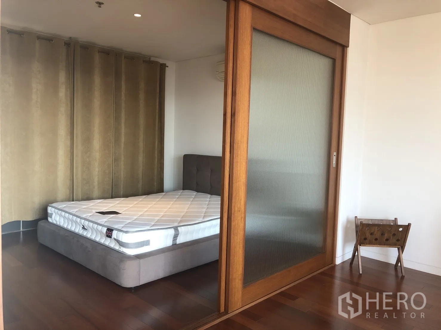 Condominium for rent in Pathum Wan, Bangkok - Bedroom seen through a wooden-framed sliding glass door with full-length curtains and hardwood floors.