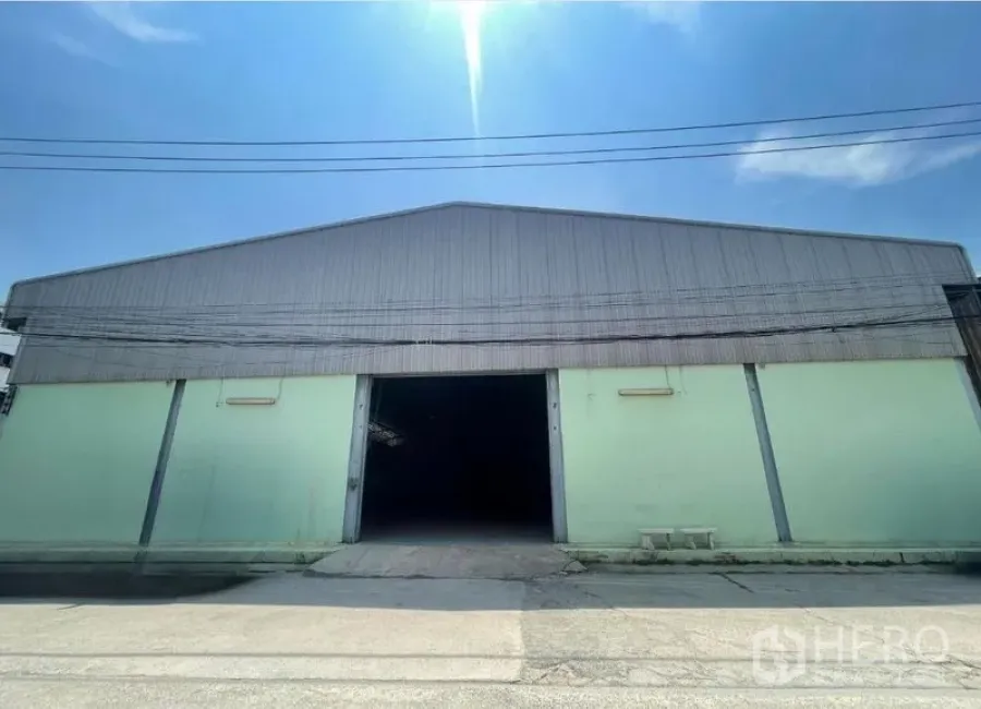 Warehouse for rent in Bang Phli, Samut Prakan - Facade of a metal-roof warehouse with an open central door under a clear blue sky.