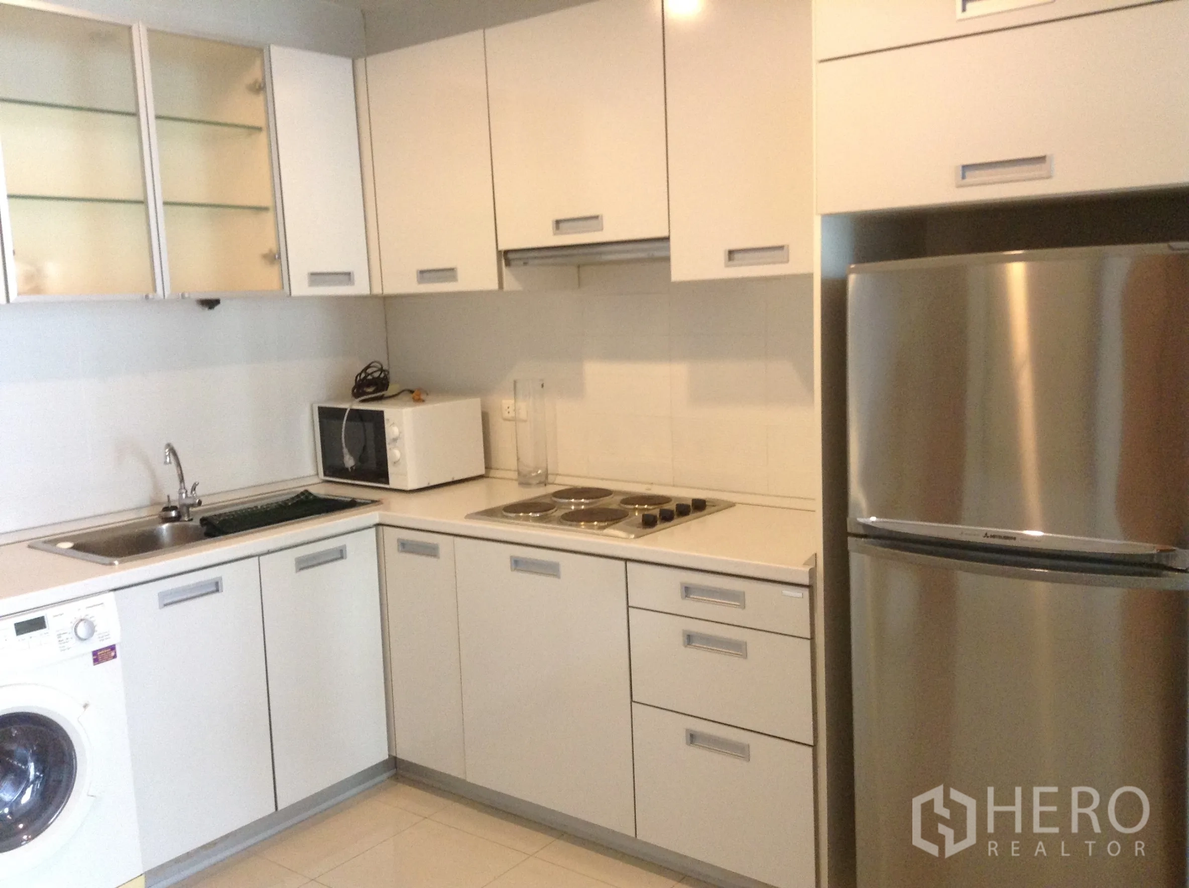 公寓 出租或出售在Khlong San, Bangkok - L形白色厨房，配电炉灶、微波炉、洗衣机和不锈钢冰箱。