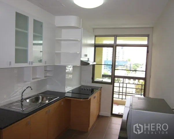 Condominium for rent or sale in Watthana, Bangkok - Kitchen with white cabinetry, black countertops, and door to the balcony.