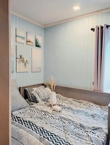 คอนโด ให้เช่าหรือขาย - ห้องนอนอบอุ่น ผนังสีฟ้าอ่อน หน้าต่างรับแสง และชุดเครื่องนอนลายกราฟิก