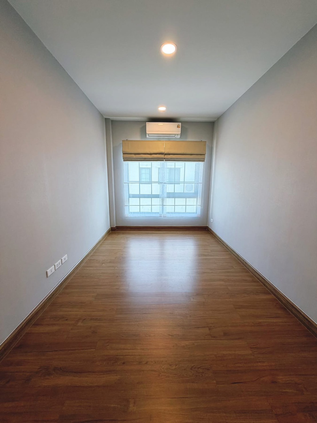 Detached House for rent in Bang Phli, Samut Prakan - Elongated empty room with wood flooring, large window, air conditioning and recessed lighting.