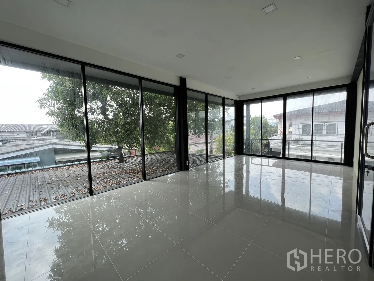 Detached House for rent or sale in Phra Khanong, Bangkok - Bright upper room with wraparound glass and glossy tile floors overlooking trees.