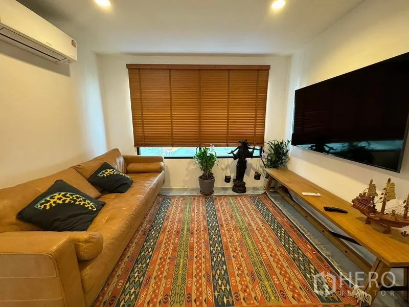 Condominium for rent or sale - Cozy living room with leather sofa, large TV, blinds, and colorful carpet.