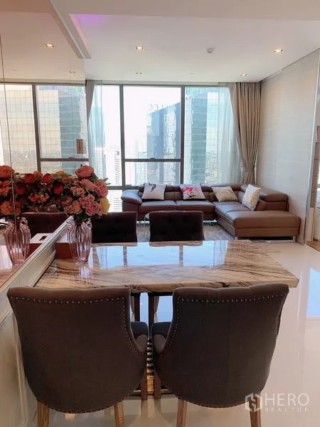 Condominium for sale - Marble dining table with plush chairs beside panoramic windows.