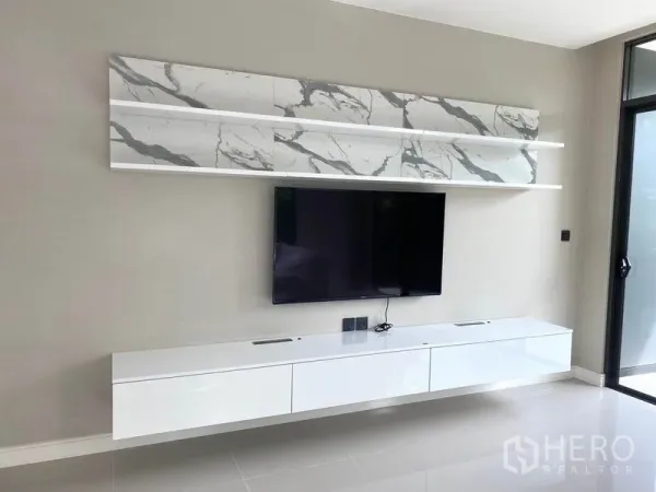 Detached House for rent in Saphan Sung, Bangkok - TV wall with mounted flat-screen, marble-look shelves and a white floating console beside a sliding door.