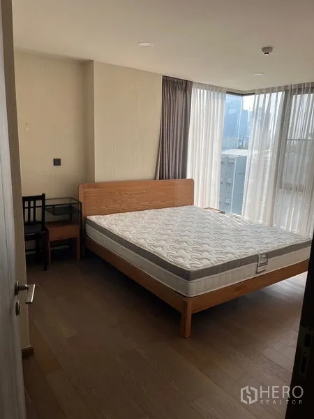 公寓 出租在Pathum Wan, Bangkok - 转角卧室，大面积落地窗与纱帘，木质床架与小书桌。