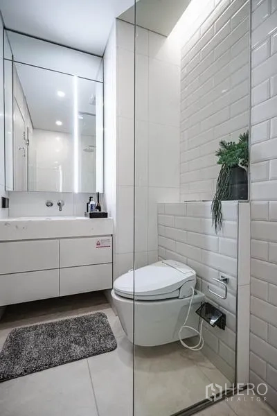 Condominium for sale in Khlong Toei, Bangkok - Contemporary bathroom with wall-mounted vanity, large mirror cabinets, toilet, and a glass shower.