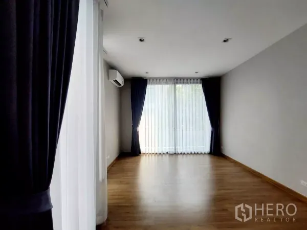 Townhouse for rent in Lat Phrao, Bangkok - Spacious bedroom with air conditioner, wooden floor and large windows providing abundant natural light.