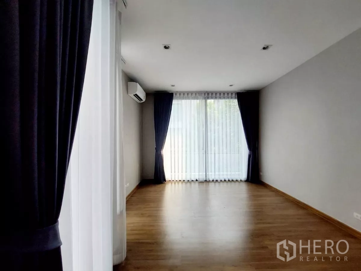 Townhouse for rent in Lat Phrao, Bangkok - Spacious bedroom with air conditioner, wooden floor and large windows providing abundant natural light.