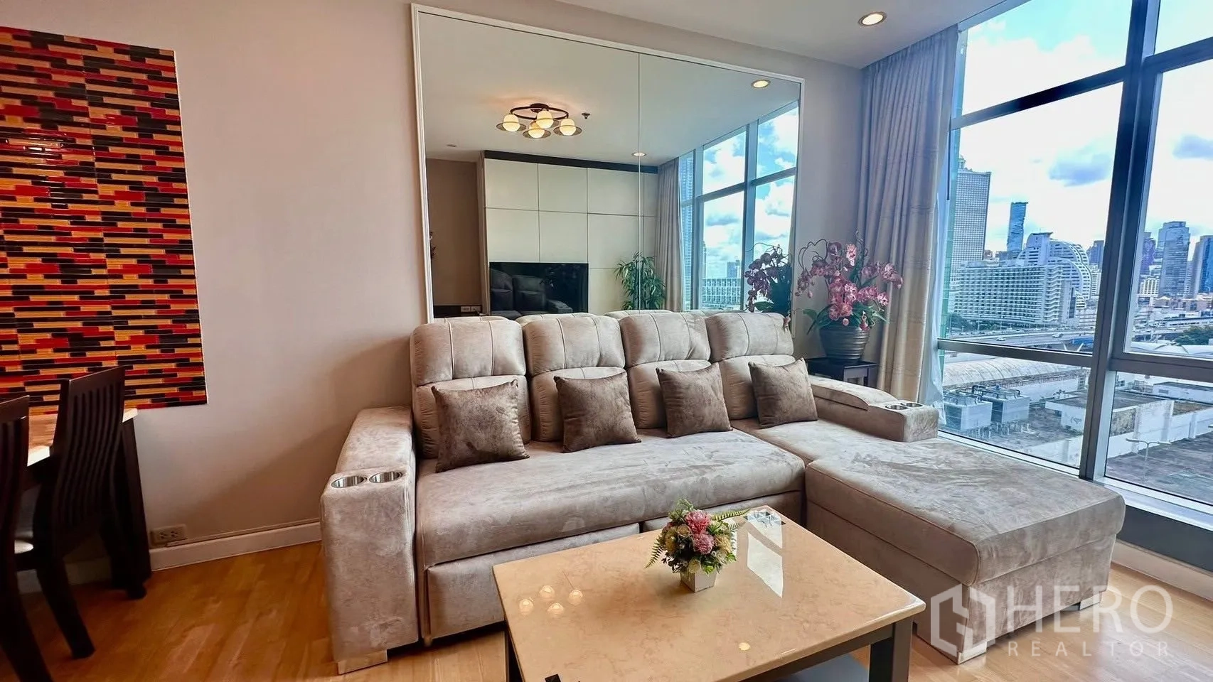 Condominium for rent in Khlong San, Bangkok - Bright living room with L-shaped sofa, coffee table, dining area, and floor-to-ceiling windows with city view.
