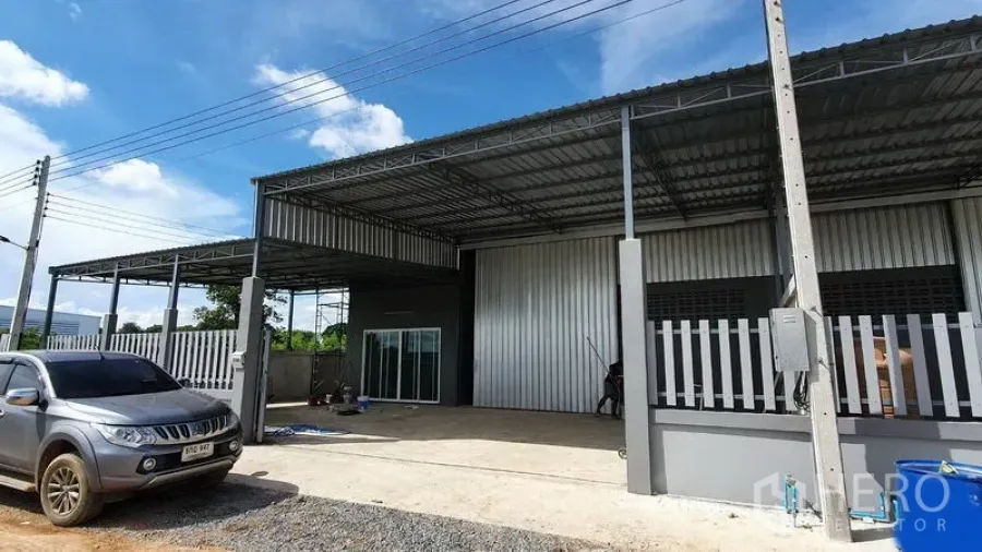 Warehouse for rent in Lam Luk Ka, Pathum Thani - Modern metal-clad warehouse exterior with covered loading bay, gated frontage and parking under clear skies.