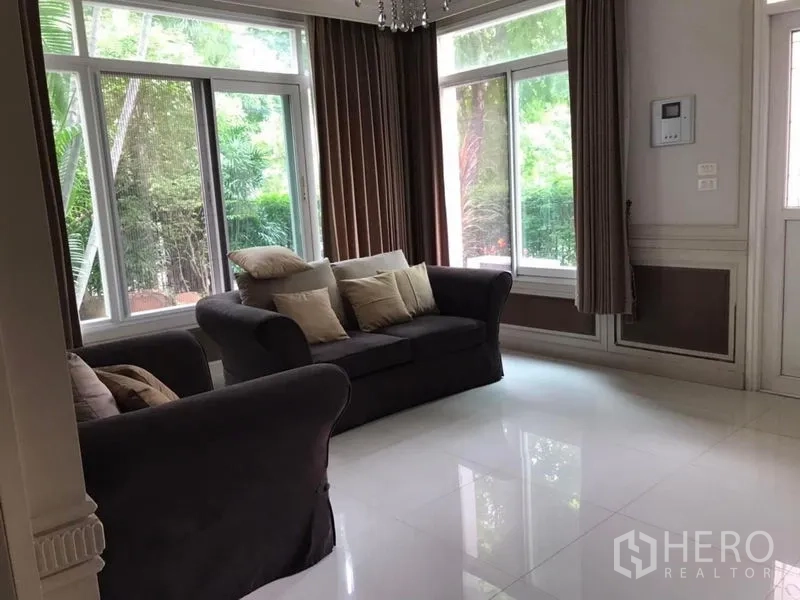 独立式住宅 出租在Bang Khen, Bangkok - 客厅配沙发与大窗，窗帘与花园景观。