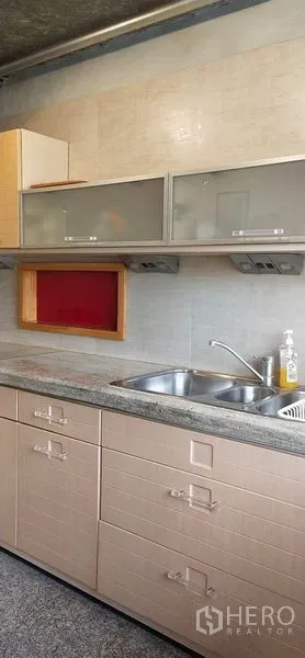 Condominium for sale in Watthana, Bangkok - Close-up of kitchen sink with frosted glass cabinets and tiled backsplash in a Sukhumvit condominium.