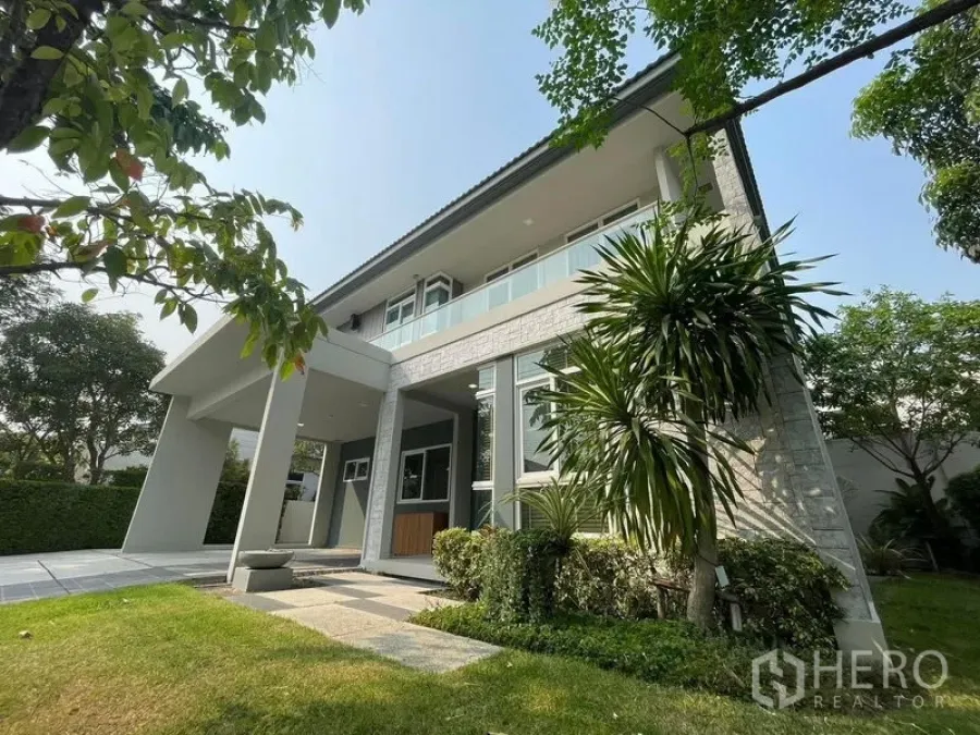 Detached House for rent in Prawet, Bangkok - Front view of a brand‑new two‑storey detached house with balcony, covered porch and landscaped lawn in a gated community.