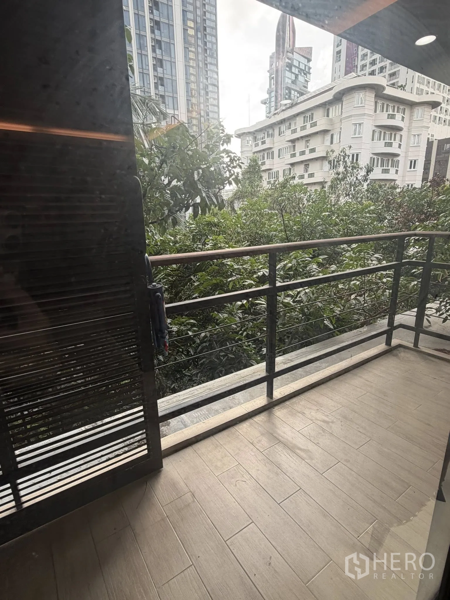 Condominium for rent in Watthana, Bangkok - Private balcony with wood-look tiles overlooking trees and city towers.