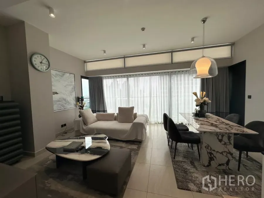 Condominium for rent in Bang Rak, Bangkok - Bright open-plan living and dining area with marble table, modern sofa, and floor-to-ceiling windows with sheer curtains.