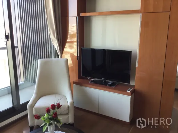 Condominium for rent in Khlong Toei, Bangkok - Cozy living area with TV unit, armchair, flowers on coffee table and balcony doors.