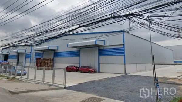 货栈 出租在Bang Phli, Samut Prakan - 路边带围栏的仓库园区，多排库门与停车位，头顶为市政电缆。
