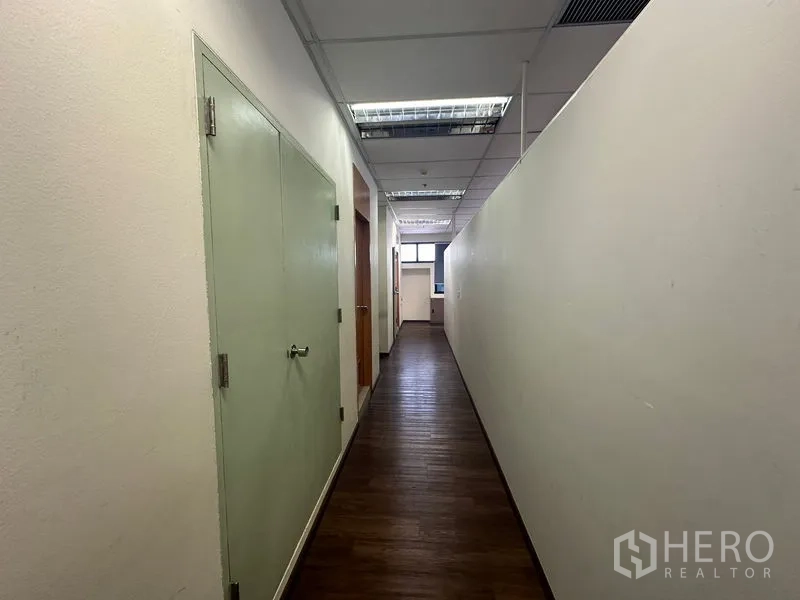 Office Space for rent in Bang Rak, Bangkok - Long corridor with wooden floors and drop-ceiling lighting inside the office.