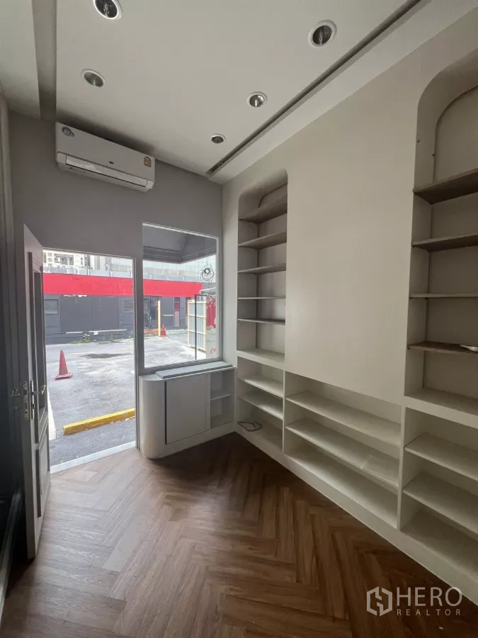 Retail Space for rent in Watthana, Bangkok - Street-facing shop with glass storefront, air conditioner, and wall shelving opening to a parking area.