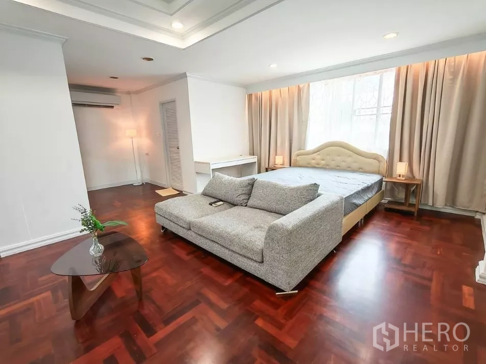 Detached House for rent in Yan Nawa, Bangkok - Bedroom with gray loveseat at the foot of a bed and polished wood floors.