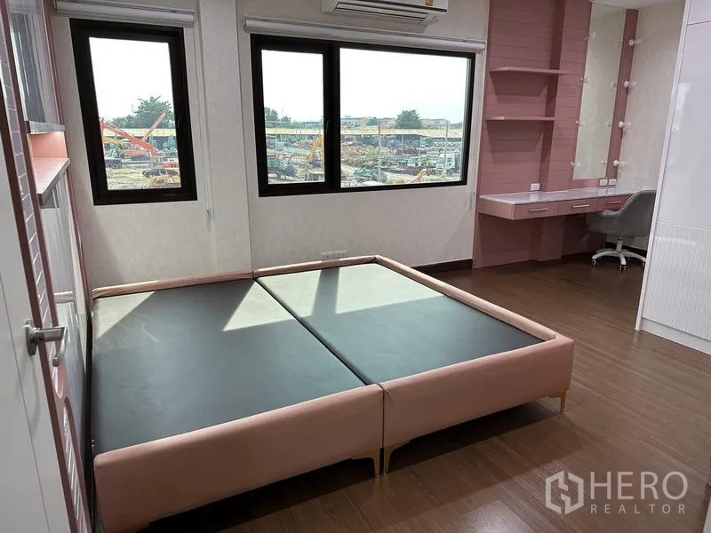 Detached House for sale in Saphan Sung, Bangkok - Sunlit bedroom with large windows, pink bed and work desk overlooking the neighborhood.