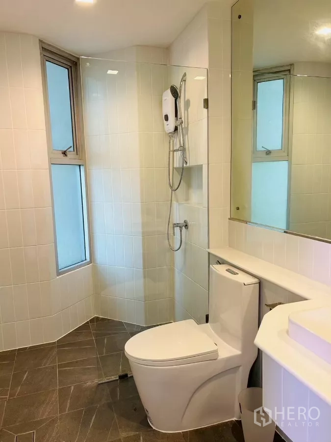公寓 出租在Bang Rak, Bangkok - 整洁的瓷砖浴室，玻璃淋浴房、热水器、大镜与座厕。
