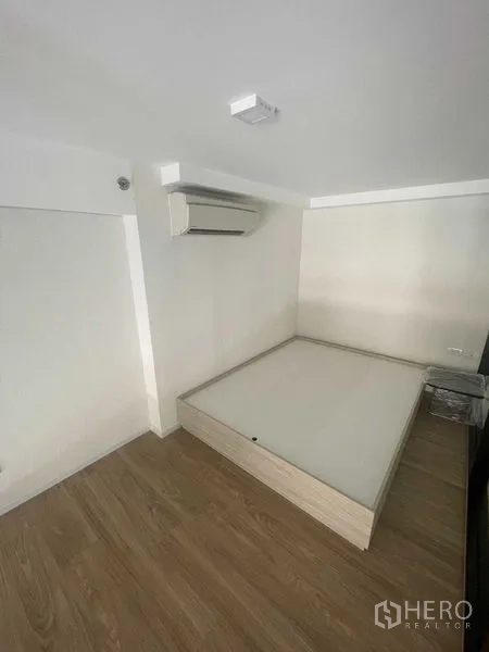 Condominium for rent in Khlong Toei, Bangkok - Cozy bedroom nook with platform bed and air conditioner on wood flooring.