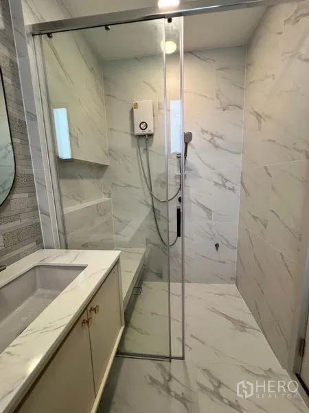 Detached House for rent or sale in Saphan Sung, Bangkok - Marble-tiled shower room with glass enclosure and a sleek vanity.