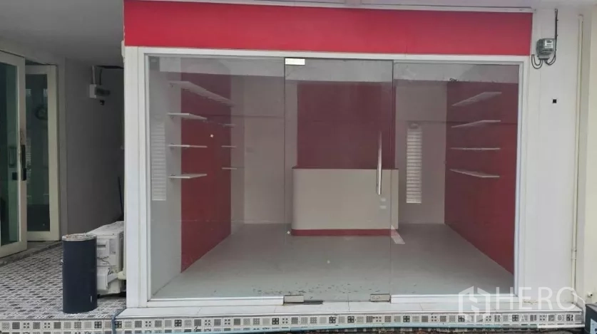 零售空间 for rent in Watthana, Bangkok - 临街店铺外立面为整面玻璃，顶部红色招牌板，室内展示架可见。
