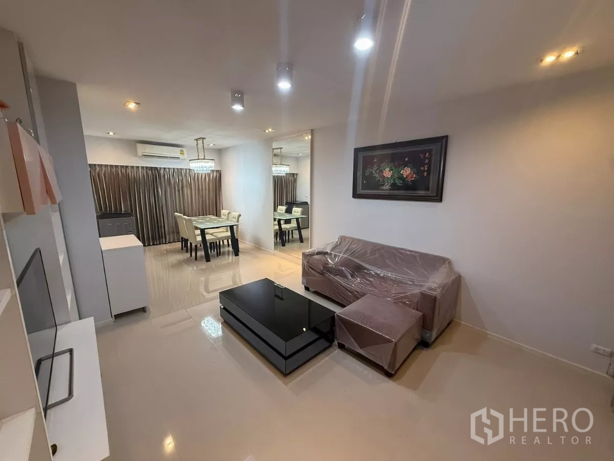 Townhouse for rent in Suan Luang, Bangkok - Bright lounge with mirrored wall, sectional sofa and black coffee table beside dining space.