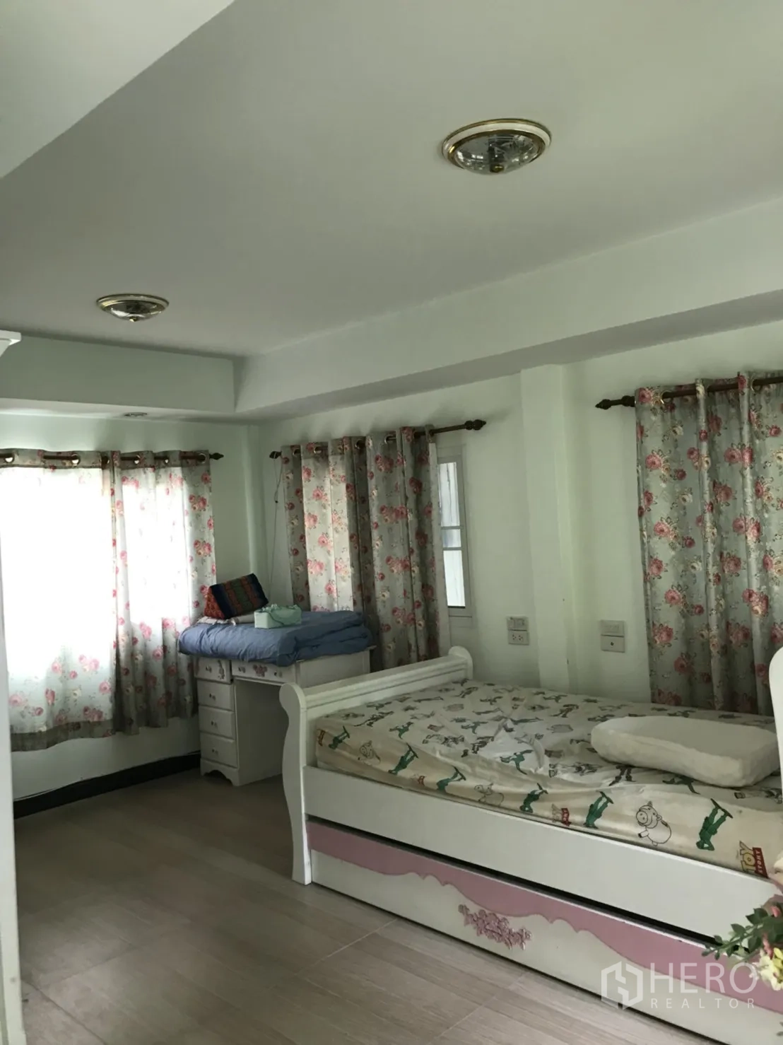Detached House for rent in Lat Krabang, Bangkok - Furnished bedroom with white daybed, desk and floral curtains allowing ample natural light.