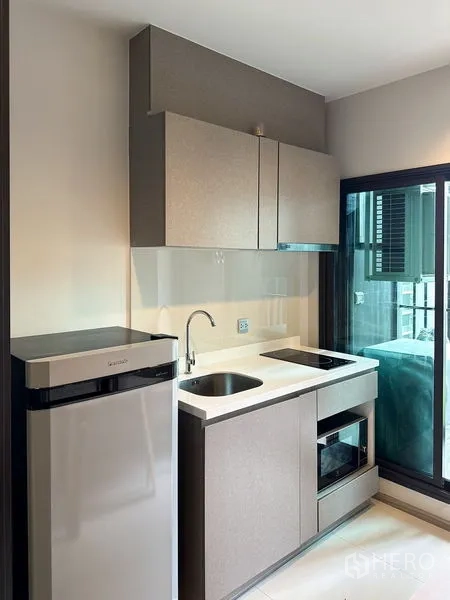 公寓 出售在Ratchathewi, Bangkok - 紧凑小厨房，配冰箱、水槽、吊柜、炉灶与微波炉，旁为玻璃门。