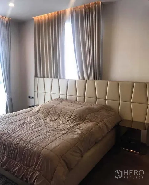 Condominium for rent or sale in Watthana, Bangkok - Primary bedroom with padded headboard, soft lighting and tall curtains.