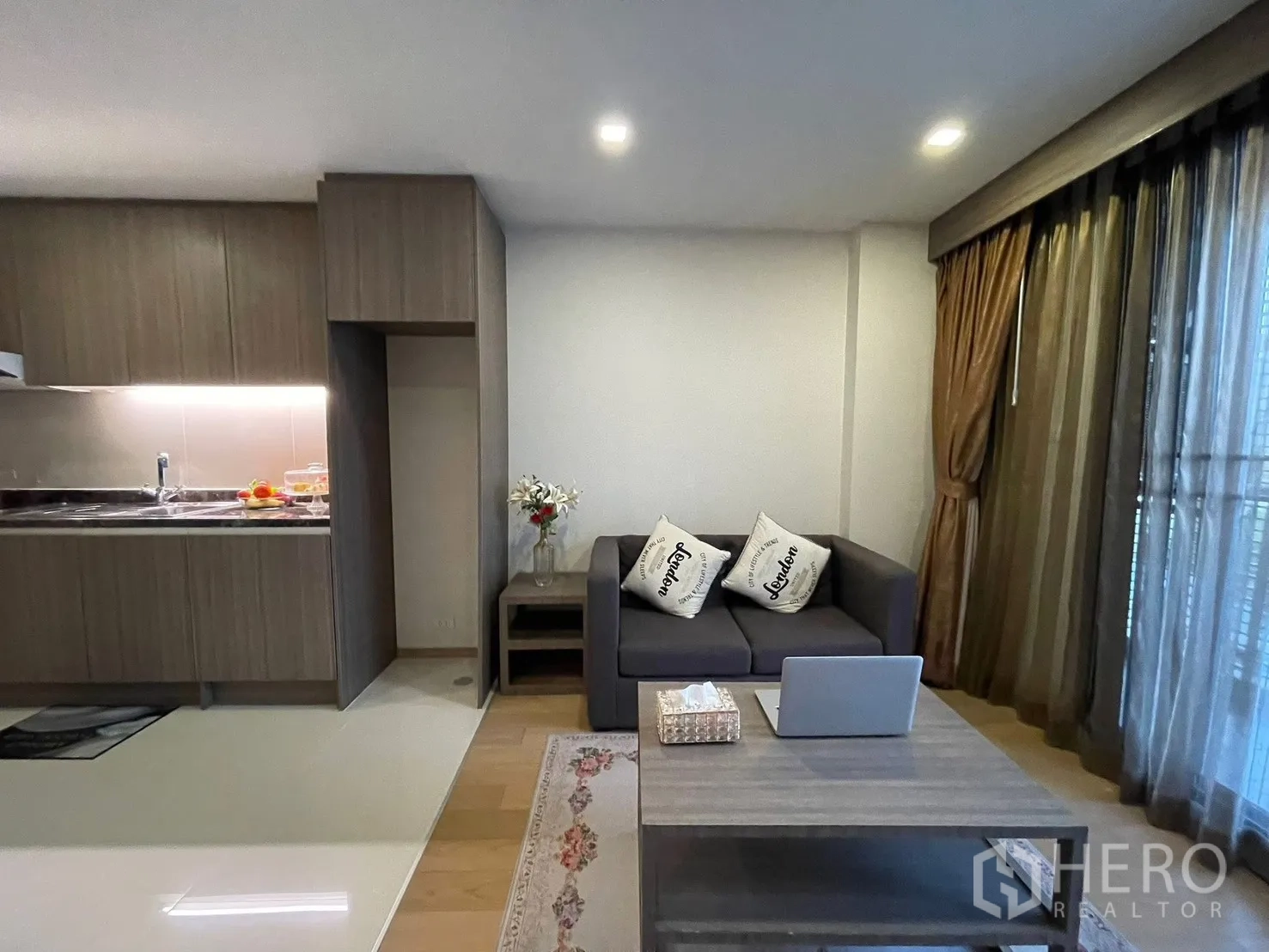 คอนโด for rent in Watthana, Bangkok - พื้นที่นั่งเล่นโอเพ่นแปลนพร้อมโซฟาสีเทา โต๊ะกลาง และครัวบิลท์อินโทนไม้มีไฟใต้ตู้