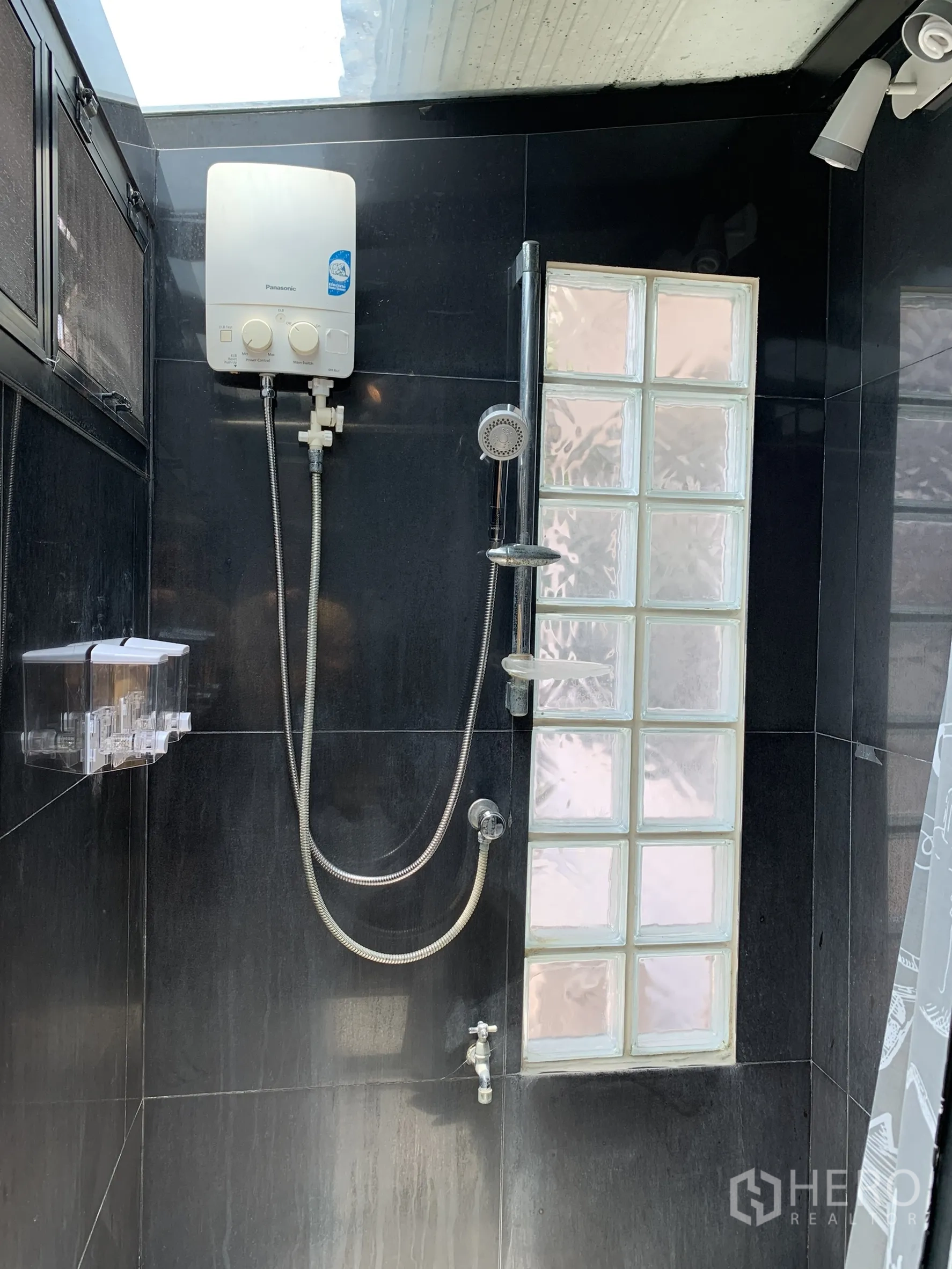 独栋房屋 for rent in Saphan Sung, Bangkok - 深色瓷砖浴室，玻璃砖窗与手持花洒、热水器及天窗采光。