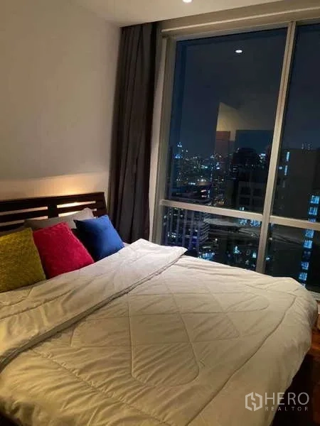 คอนโด ขายในSathon, Bangkok - ห้องนอนหลักยามค่ำ เห็นแสงไฟเมืองผ่านหน้าต่างสูงและผ้าม่าน.