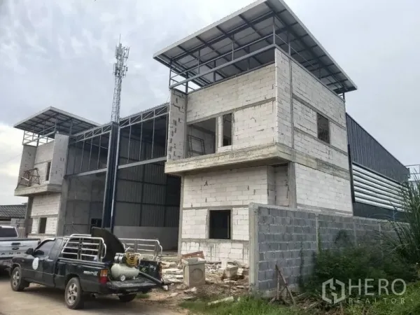 Warehouse for rent in Lam Luk Ka, Pathum Thani - Street-side view of warehouse facade with parking area and construction materials.