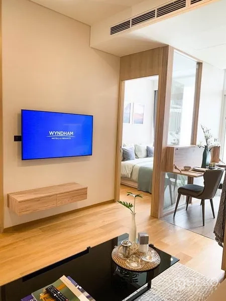 Condominium for sale in Khlong Toei, Bangkok - Living room with wall-mounted TV, wood floors, and a sliding glass partition leading to the bedroom and dining area.