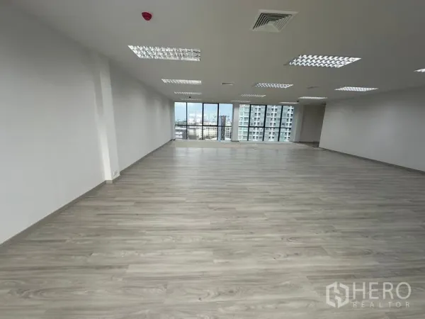Office Space for rent - Open-plan office with light wood floors, drop ceiling lights, and full-height windows with city views in Din Daeng, Bangkok.