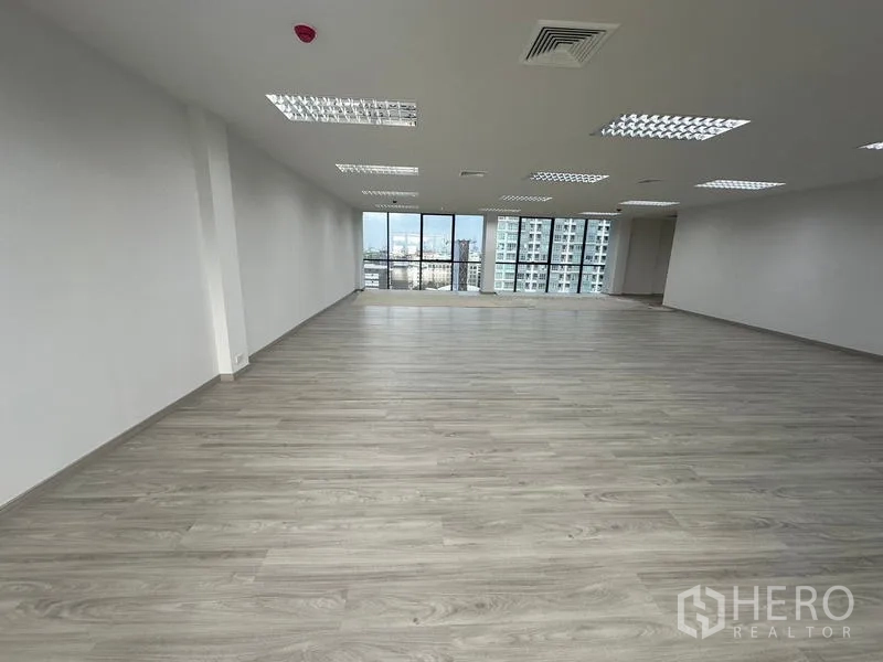 Office Space for rent - Open-plan office with light wood floors, drop ceiling lights, and full-height windows with city views in Din Daeng, Bangkok.