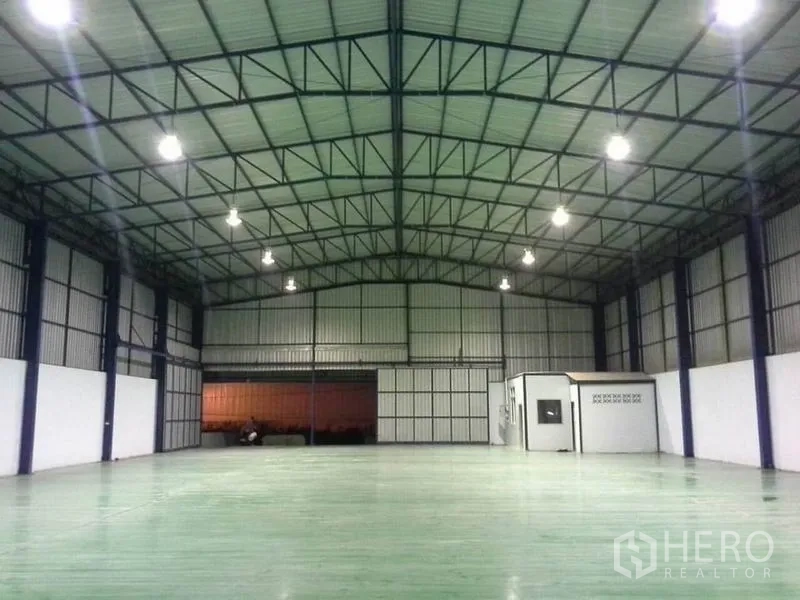 Warehouse for rent in Chon Buri - Open-plan warehouse interior with small office room, high ceiling, roller shutter doors and epoxy flooring.