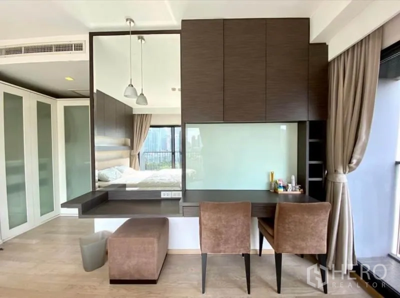 Condominium for rent in Khlong Toei, Bangkok - Built-in study area with two chairs, upper cabinets, and mirror beside full-height curtains.