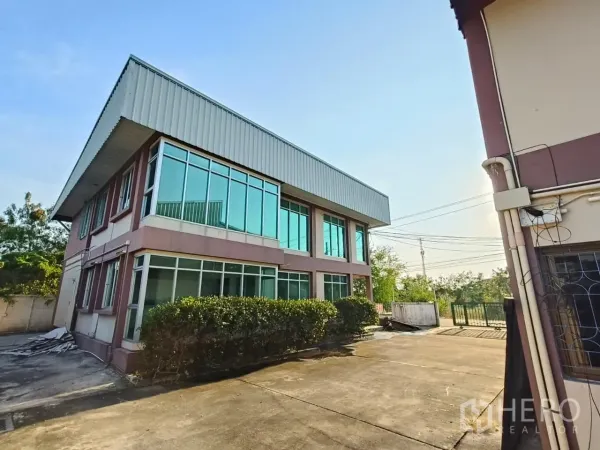 คลังสินค้า ให้เช่าหรือขายในMin Buri, Bangkok - อาคารออฟฟิศกระจกมุมเชื่อมต่อโกดัง หน้าต่างบานใหญ่ ลานคอนกรีตกว้าง และประตูรั้วสีเขียว